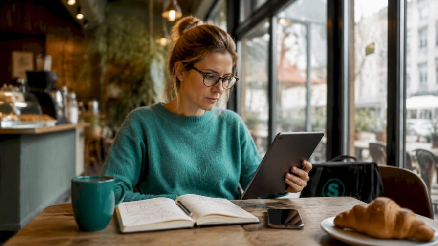Een SEA-specialist zit geconcentreerd aan zijn bureau, omringd door twee beeldschermen en een tablet, helemaal klaar om campagnes te optimaliseren.